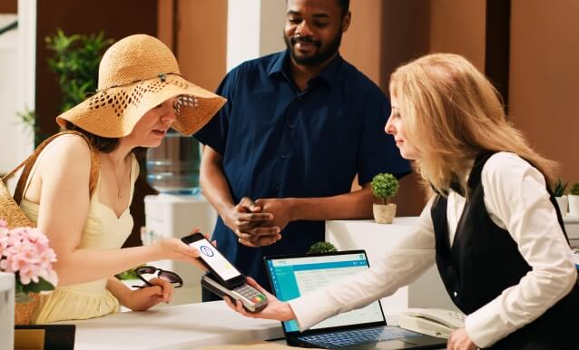 donna con cappello che paga in hotel appoggiando lo smartphone sul POS gprs