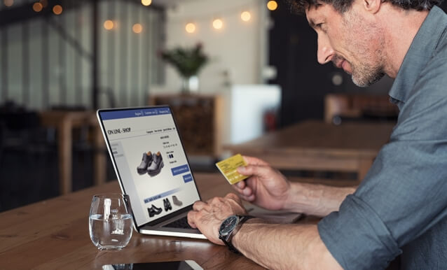 Un uomo è seduto al computer portatile, mentre acquista un paio di scarpe, mostrando interesse e attenzione.