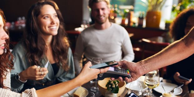 Un gruppo di persone sedute a un tavolo, utilizzando i loro telefoni per effettuare pagamenti contactless.