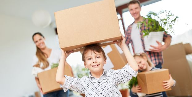 Un bambino e la sua famiglia stanno traslocando, circondati da scatole e un'atmosfera di gioia.