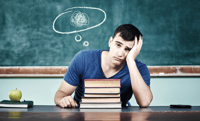 studente seduto alla cattedra con dei libri davanti a sè, in atteggiamento confuso