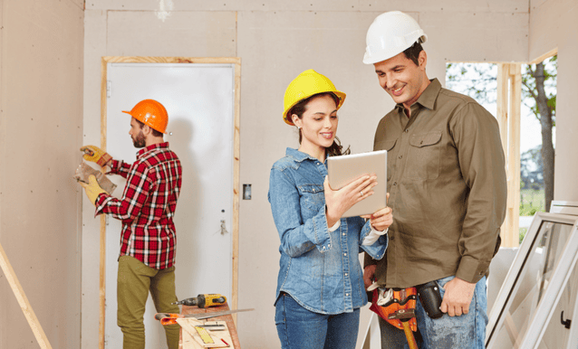 Uomo e donna in caschi da cantiere, in un ambiente con materiali di costruzione