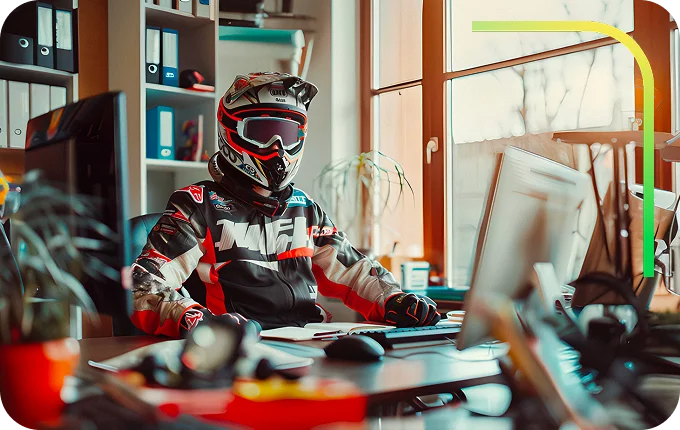 ragazzo vestito da motociclista seduto su una scrivania che sta lavorando al pc