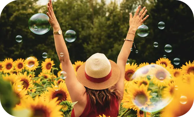 ragazza che gioisce con le braccia verso il cielo in mezzo ad un campo di girasoli e con delle bolle